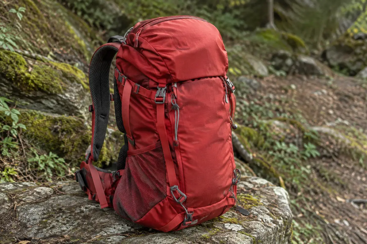 Sac à dos de randonnée rouge pliable posé sur une pierre en sous-bois, poches et bretelles visibles
