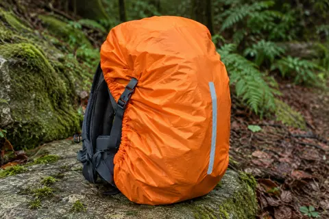 Housse de pluie orange avec bande réfléchissante installée sur un sac à dos de randonnée en sous-bois.