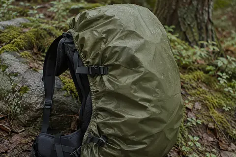 Housse de pluie vert olive ajustée sur un sac à dos de randonnée dans un sous-bois humide