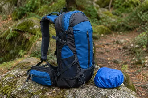 Sac à dos de randonnée bleu saphir et noir posé sur une pierre, avec ses poches et bretelles visibles