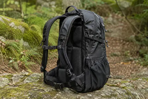 Sac à dos de randonnée noir posé sur une pierre, avec ses bretelles rembourrées et ses poches latérales visibles
