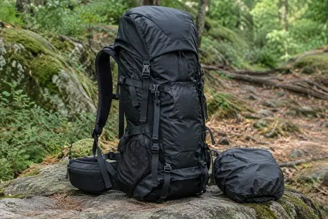 Sac à dos de trekking noir avec poches latérales, sangles de compression et housse de pluie en sous-bois