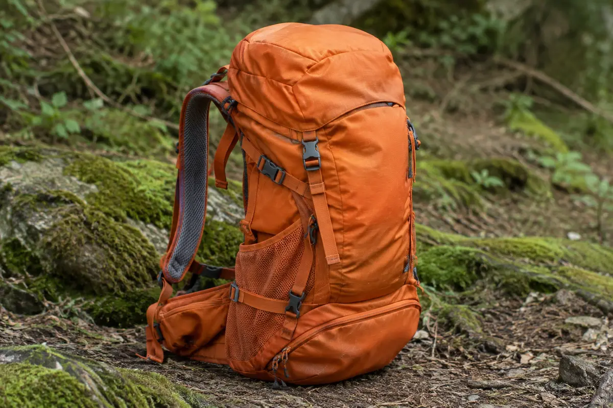 Sac à dos de randonnée orange pliable de 40 L posé sur un sentier, avec un compartiment inférieur pour chaussures