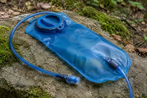 Poche à eau bleue de 2 L avec tube amovible posée sur une pierre près d’un sentier forestier