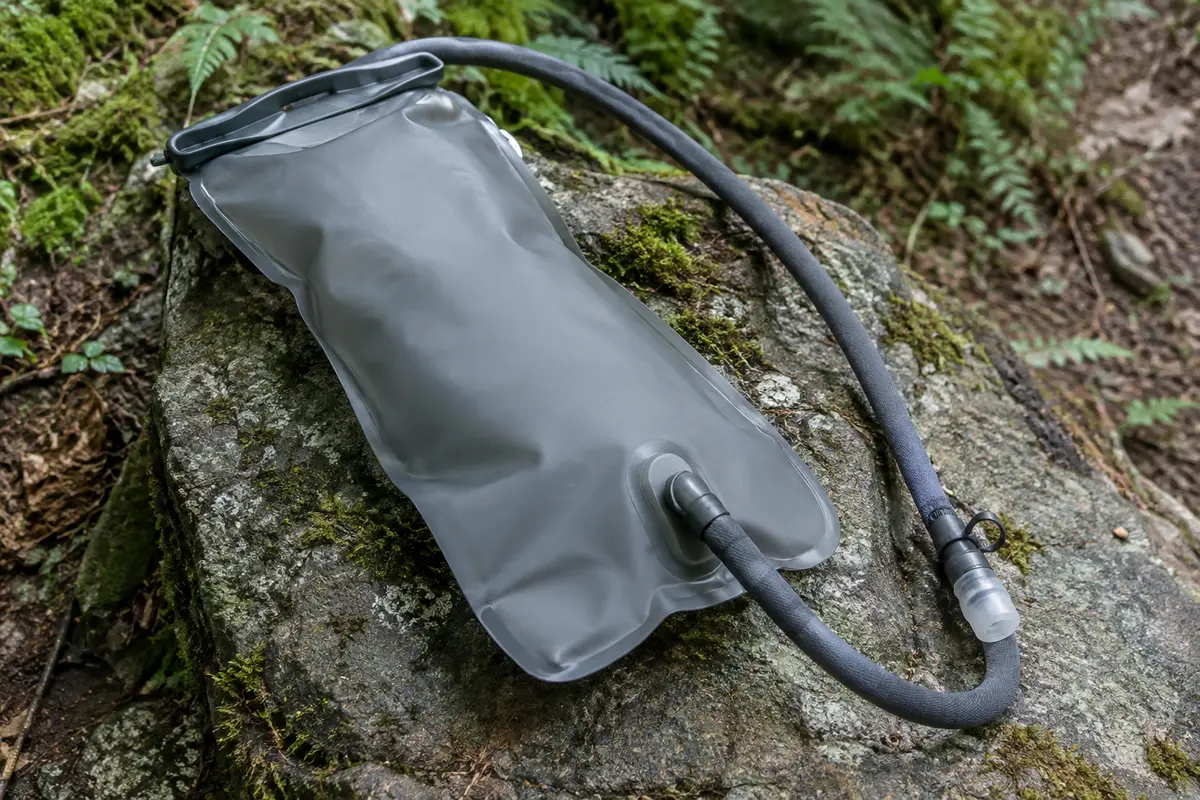Poche à eau grise de 3 L avec tube isolé et valve en silicone, posée sur une pierre en sous-bois.