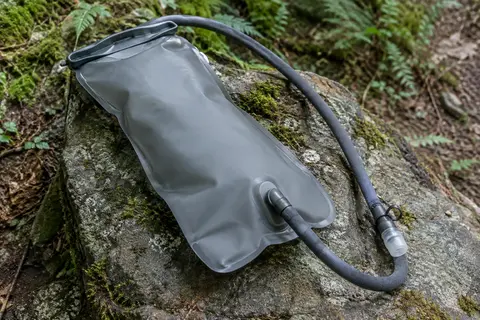 Poche à eau grise de 3 L avec tube isolé et valve en silicone, posée sur une pierre en sous-bois.
